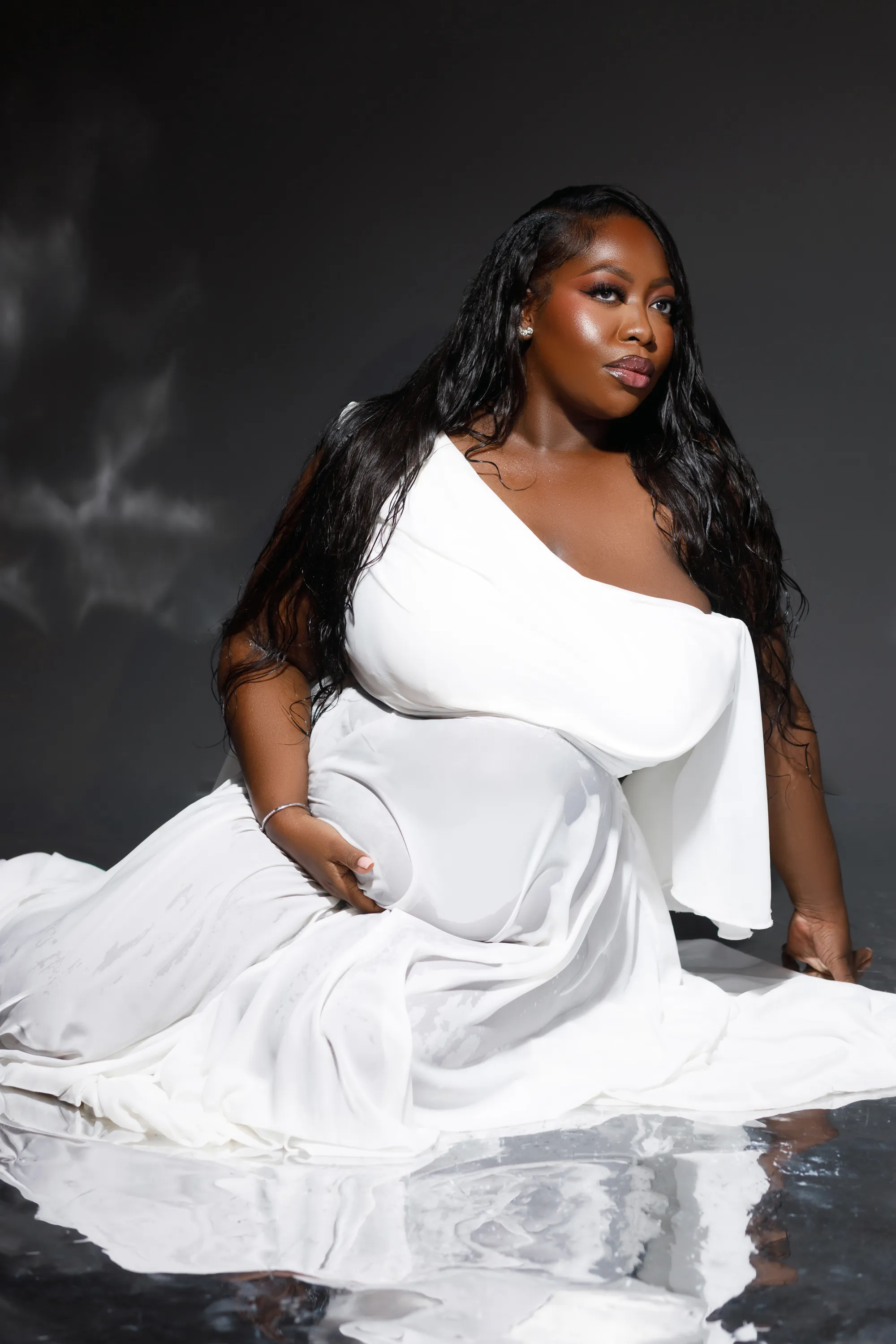 Elegant maternity portrait of a woman in a flowing white dress cradling her belly.